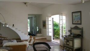 A spacious living area with a high ceiling, a staircase leading to a balcony, and a view of greenery outside. - Large villa with pool (Saint-Paul-En-Forêt)