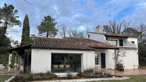 A white building with a tiled roof, a large glass door, and a small garden area. - Large villa with pool (Saint-Paul-En-Forêt)
