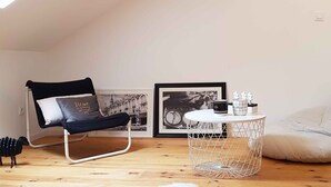 Ein modernes Wohnzimmer mit einem schwarzen Ledersessel, einem weißen Sitzsack, einem runden Drahttisch und zwei gerahmten Bildern an der Wand.