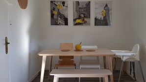 Ein Essbereich mit einem Holztisch, Stühlen und einer Bank. Über dem Tisch hängen drei gerahmte Bilder an der Wand.