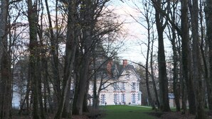 Polku johtaa suureen, historialliseen rakennukseen, jonka ympärillä on korkeita puita.