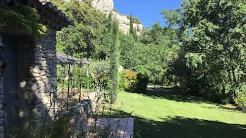 Un bâtiment en pierre surmonté d’un toit de tuiles, entouré d’une végétation luxuriante et s’ouvrant sur un ciel bleu azur.