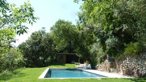 A rectangular swimming pool surrounded by a well-maintained lawn, with a stone wall and a small wooden structure in the background. - Cottage 2 pers.Pets welcome, quiet location, south facing.  Swimming pool. (LE BEAUCET)