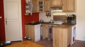 A compact kitchen with wooden cabinets, a dishwasher, a stove, and a coffee maker. - Cottage 2 pers.Pets welcome, quiet location, south facing.  Swimming pool. (LE BEAUCET)