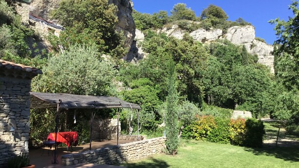 A stone building with a covered patio and a red tablecloth, surrounded by lush greenery and a mountainous backdrop. - Cottage 2 pers.Pets welcome, quiet location, south facing.  Swimming pool. (LE BEAUCET)