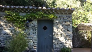 A stone building with a dark blue door, a small window, and a potted plant in front. - Cottage 2 pers.Pets welcome, quiet location, south facing.  Swimming pool. (LE BEAUCET)