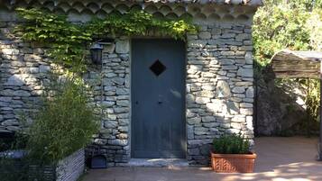 Un bâtiment en pierre avec une porte bleu foncé, une petite fenêtre et un pot de fleurs devant.