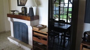 Une pièce avec une cheminée, une table entourée de chaises, une fenêtre donnant sur l’extérieur et un tableau encadré accroché au mur.