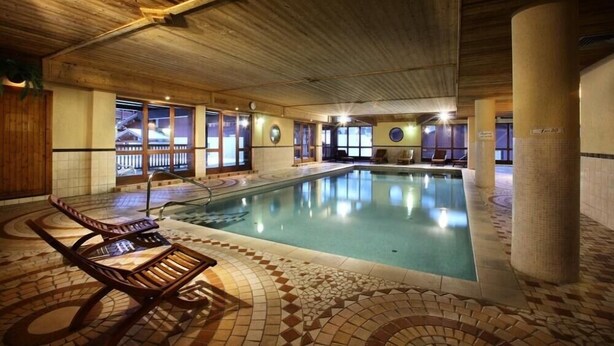 An indoor swimming pool with a tiled floor, wooden lounge chairs, and a view of the outside through large windows. - Arcs 2000, new 95m² apartment in a chalet, 2 min from the slopes, wifi, pkg (Bourg-Saint-Maurice)