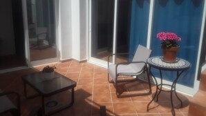 Un pati il·luminat pel sol amb una taula i caires, una planta en test i una porta corredissa de vidre que dona a un espai interior.