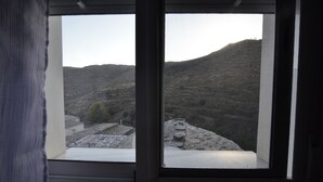 Finestra amb vista a un paisatge de muntanya, incloent camps de conreu en terrasses i una construcció de pedra.