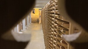 A corridor with a wall of wine bottles on the right, leading to a room with a stone wall and a bench.