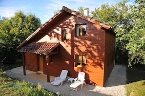 Une cabane en bois avec un toit en pente, deux fenêtres et une véranda équipée de deux fauteuils de jardin blancs.
