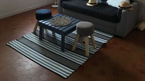 Uma sala de estar com sofá, puf e mesa de centro, um tapete estampado e uma luminária.