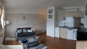 Um espaço compacto com cozinha compacta, um sofá com almofadas, uma pequena mesa de jantar e uma cama.
