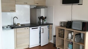 Uma cozinha compacta equipada com lava-louças, frigorífico, micro-ondas e televisão fixada na parede.