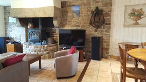 A cozy living room with a stone fireplace, a television, and comfortable seating. - Gite "Le Bocage" - sleeps 6 - rated 2 stars (SARTILLY BAIE BOCAGE)