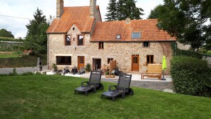 A stone building with a tiled roof, outdoor seating, and a grassy area. - Gite "Le Bocage" - sleeps 6 - rated 2 stars (SARTILLY BAIE BOCAGE)