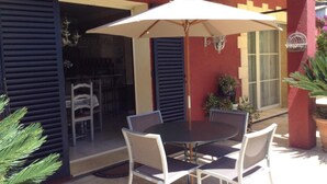 Un patio al aire libre con una mesa redonda y cuatro sillas, una sombrilla y plantas en macetas.