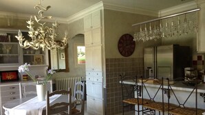 Una cocina con mesa, sillas, una araña, un reloj y una estantería para vinos.