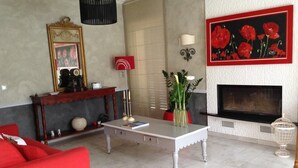 Una sala de estar con chimenea, un sofá rojo, una mesa de centro blanca y un cuadro de flores rojas.