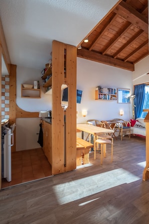 A cozy, open-plan living space with a wooden dining area, a kitchen, and a seating area with a sofa and bookshelves. - Arc 1800 apartment with mezzanine 5 people very beautiful view (Arc 1800)