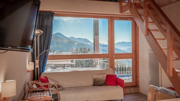 Una habitación acogedora con sofá, sillas, televisor y un amplio ventanal con vistas a la montaña.