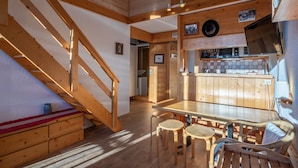 Un interior de madera con una escalera, una zona de comedor con taburetes y una cocina con armarios de madera.