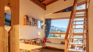 Una habitación amplia con techo y escalera de madera, un sofá, una mesa de comedor con sillas y una estantería.