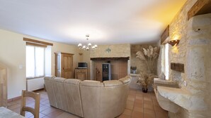 A spacious living area with a large beige sofa, a fireplace, stone walls, and a dining area with a table and chairs. - Character house in the countryside. (Les Arques)