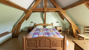 A bedroom with a sloped ceiling, wooden beams, a bed with a colorful quilt, two bedside tables with lamps, a wooden chair, and a small table. - Character house in the countryside. (Les Arques)