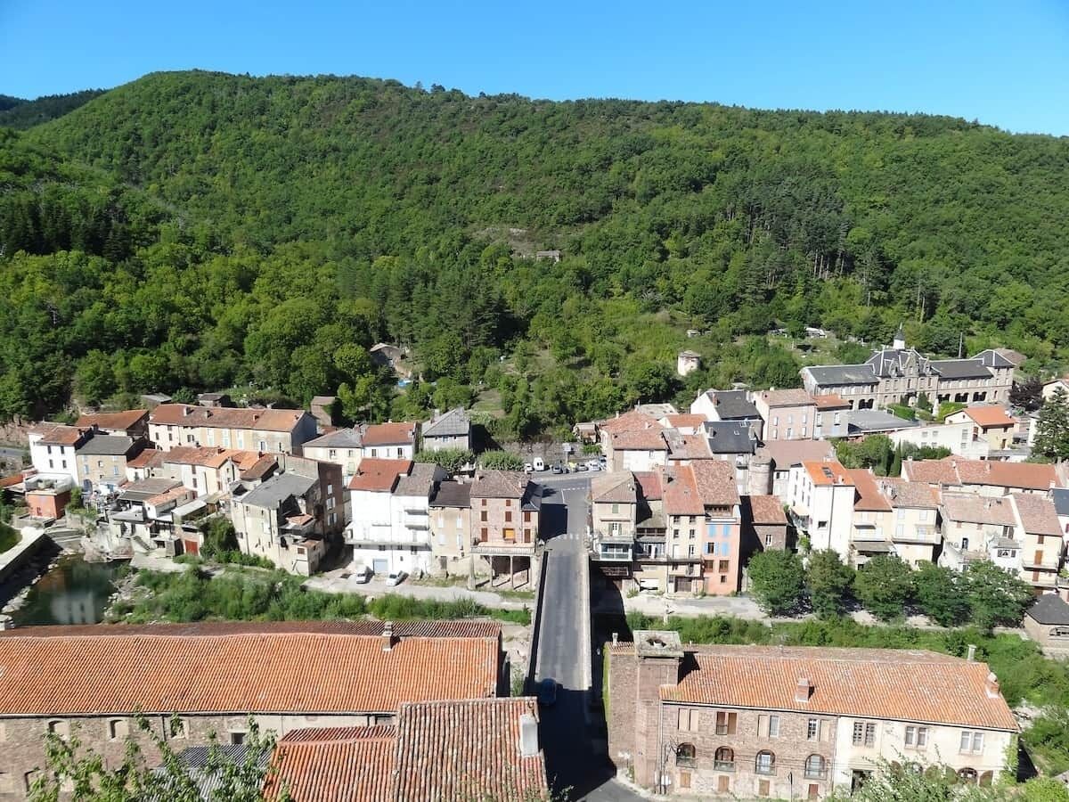 Une ville dotée de bâtiments historiques, traversée par une rivière, avec une colline boisée en arrière-plan.