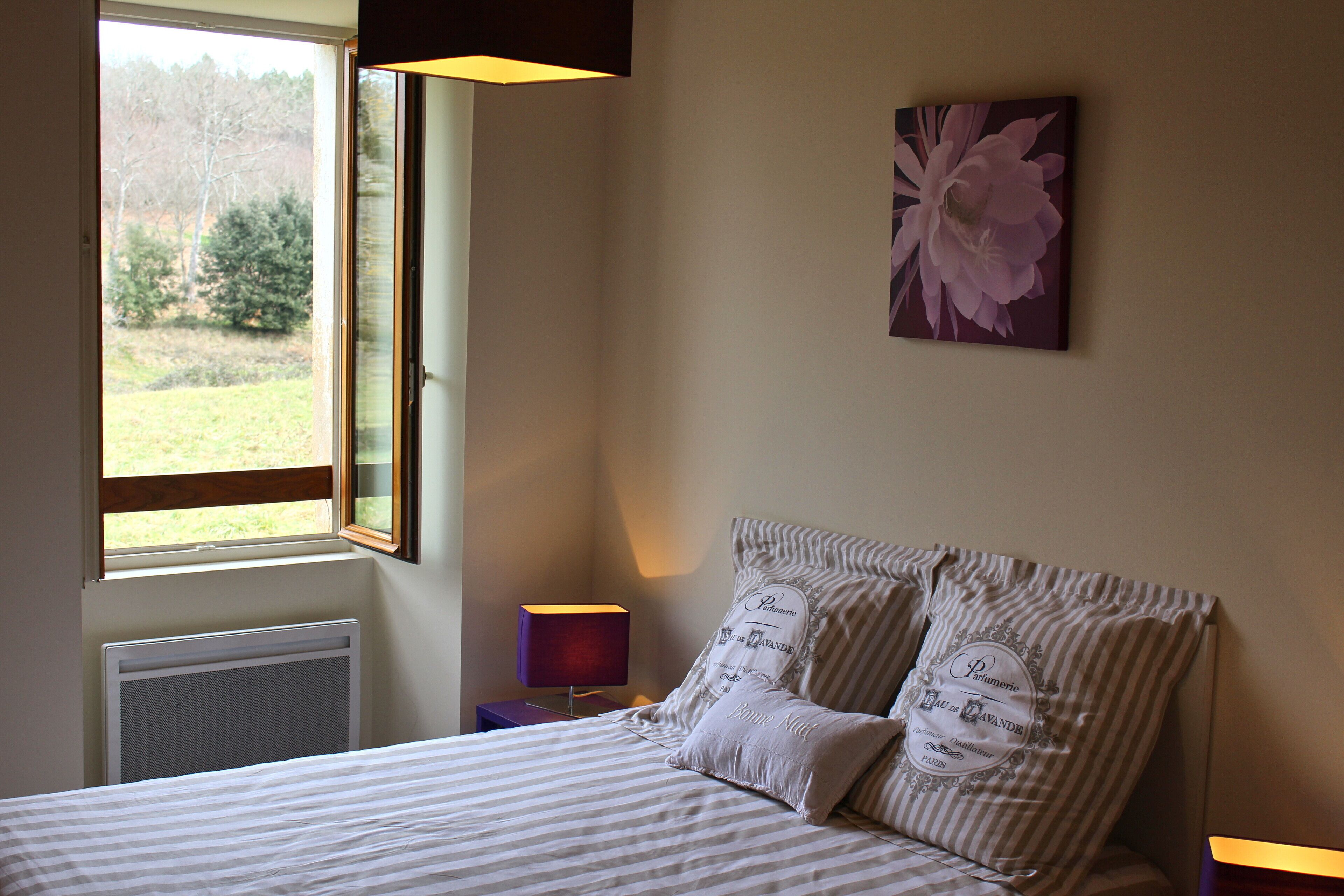 A bedroom with a bed, a window, a radiator, a nightstand, and a wall-mounted lamp.