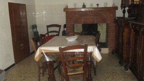 Comedor con una mesa dispuesta para seis personas, rodeada de sillas de madera. Se observa una chimenea de ladrillo al fondo.