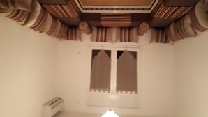 A room with a wooden ceiling, a window with curtains, and a white wall. - Air-conditioned apartment saidia (Saïdia)