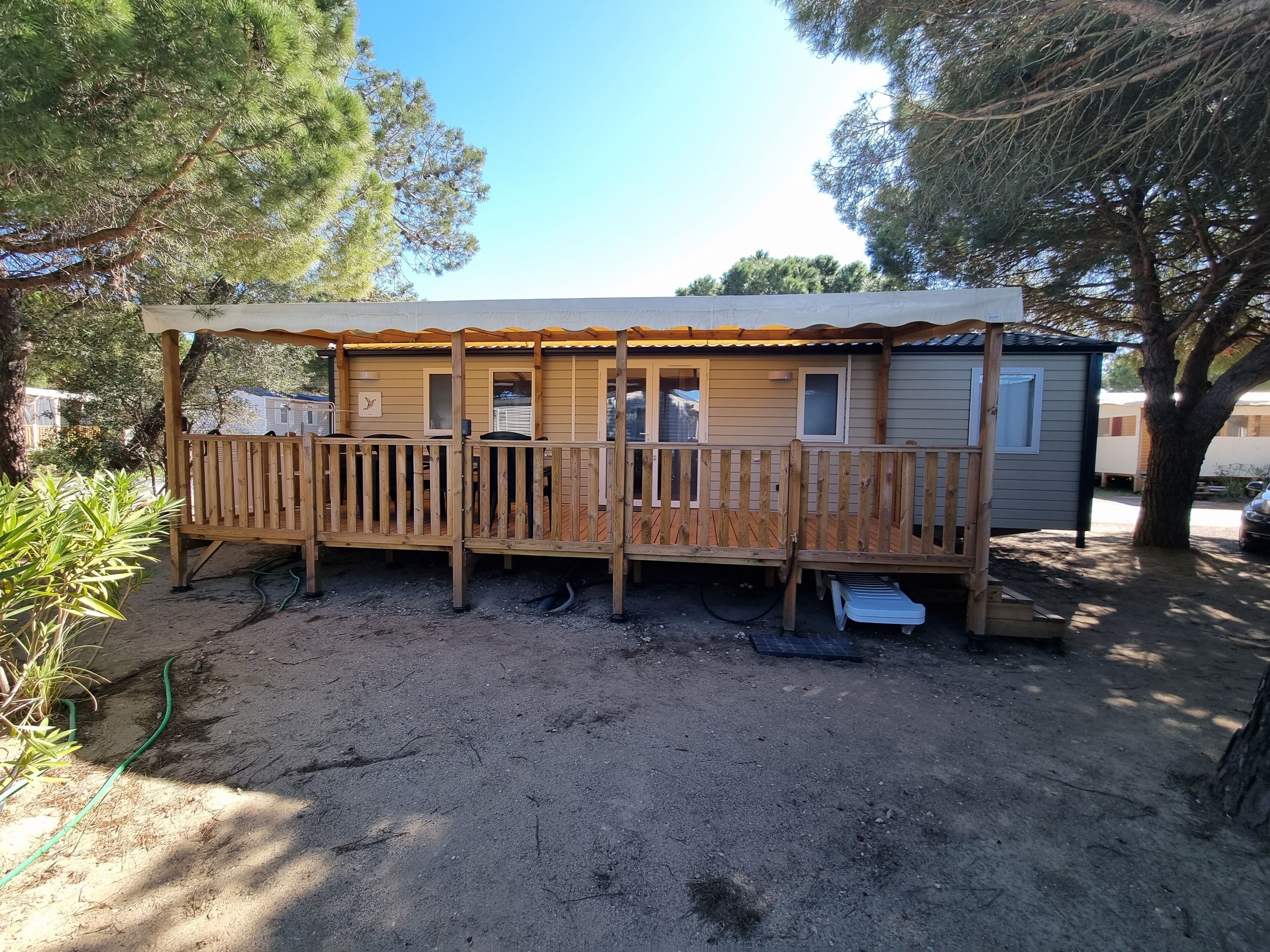 A wooden mobile home with a covered porch, a small attached shed, and a dirt ground.