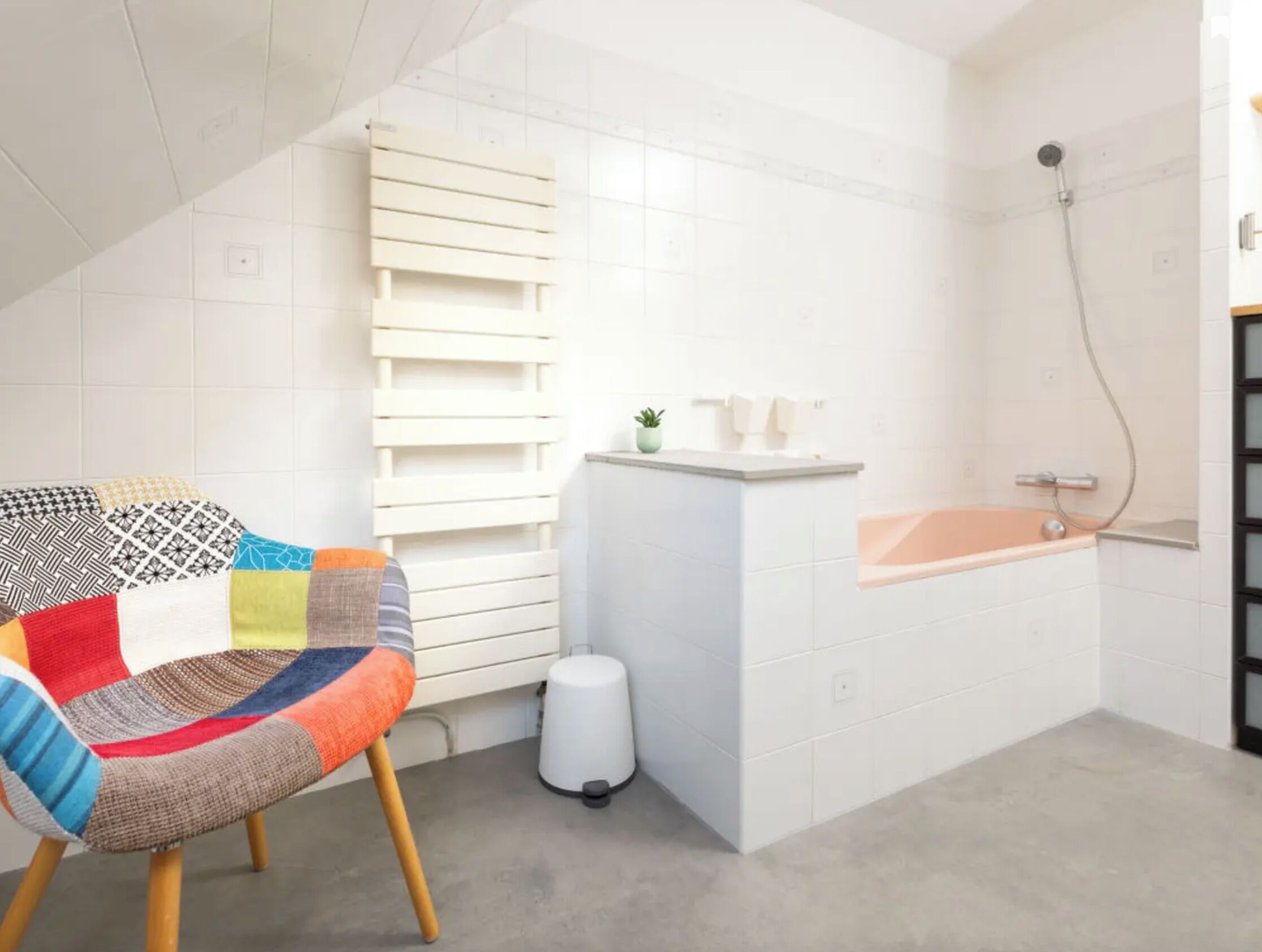 A modern bathroom with a bathtub, a shower, and a toilet. There is a colorful chair and a small plant on the counter.
