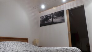 A bedroom with a bed, a nightstand, a wall-mounted lamp, and a door leading to another room. - Studio in a park near Chambord (ST LAURENT NOUAN)