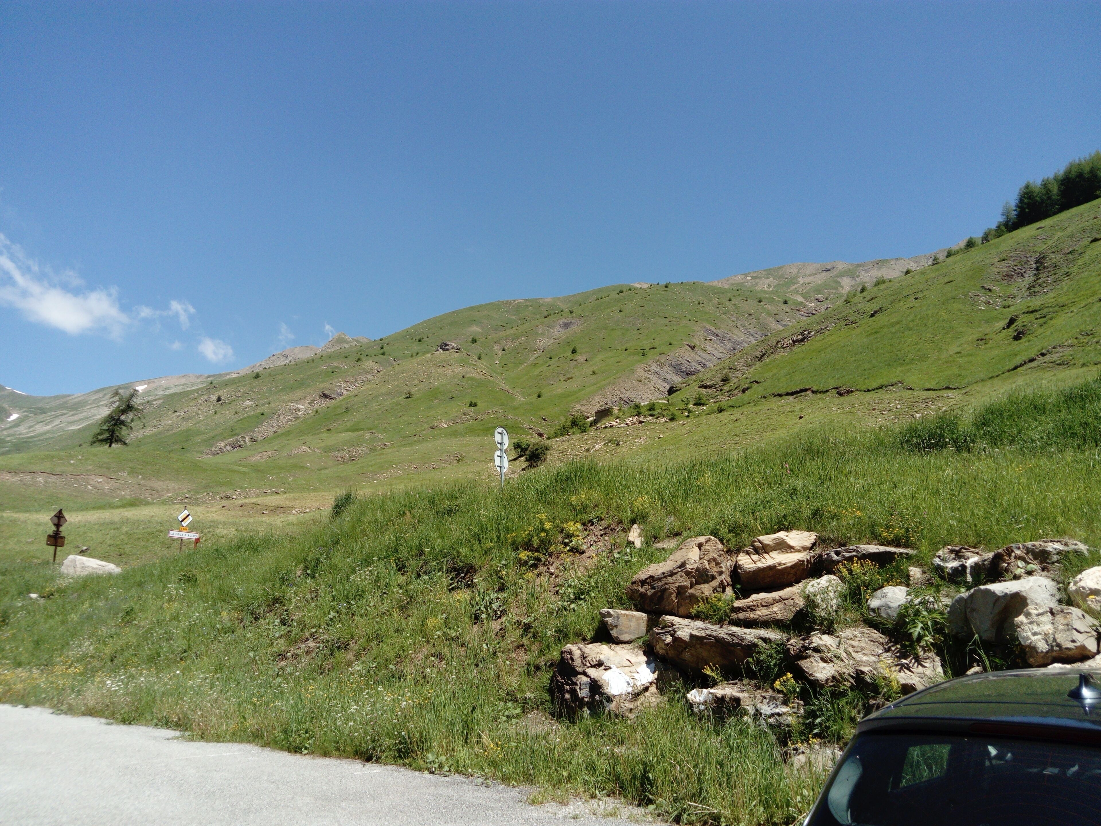 Una strada con un affioramento roccioso e un cartello stradale in una zona collinare e erbosa.