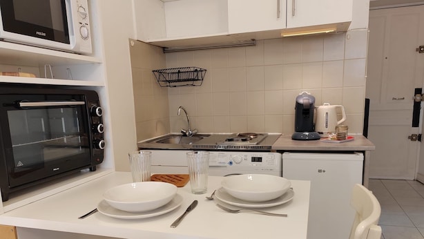 Kompakti keittiö, jossa on mikroaaltouuni, uuni, pesuallas ja kahvinkeitin. Keittiössä on myös ruokapöytä, jossa on lautasia ja ruokailuvälineitä.
