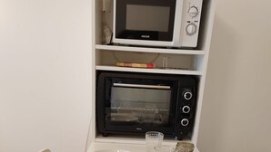 Ruokailutilassa on valkoinen pöytä, joka on katettu kahdelle, sekä mikroaaltouuni ja sen yläpuolella oleva uuni.