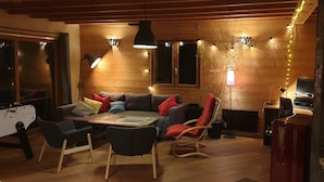 A cozy living room with wooden walls, a sofa, chairs, a coffee table, and a fireplace. - Comfortable, quiet chalet (Les Adrets)