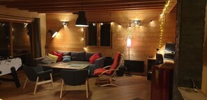 A cozy living room with wooden walls, a sofa, chairs, a coffee table, and a fireplace. - Comfortable, quiet chalet (Les Adrets)