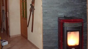 A room with a stone wall, a wooden ceiling, and a red wood-burning stove. - Comfortable, quiet chalet (Les Adrets)