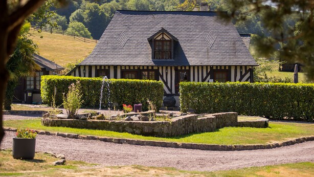 A traditional half-timbered building with a stone foundation, surrounded by well-maintained hedges and a gravel path.