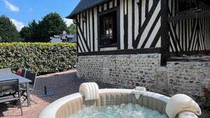 A hot tub in front of a Tudor-style house with a stone wall and a window.