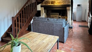A rustic interior with a wooden staircase, a stone fireplace, a sofa, and a dining table.