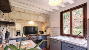 A kitchen with a stone wall backsplash, a stove, a sink, and a window with a view of trees.