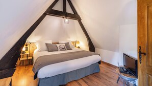 A bedroom with a sloped ceiling, a bed with a gray blanket, bedside lamps, and a TV on a small table.