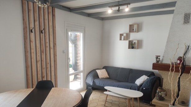 A modern living room with a dining area, featuring a wooden slat wall, a gray sofa, and a small coffee table. - MAISONETTE T2 30 M2 (Carpentras)